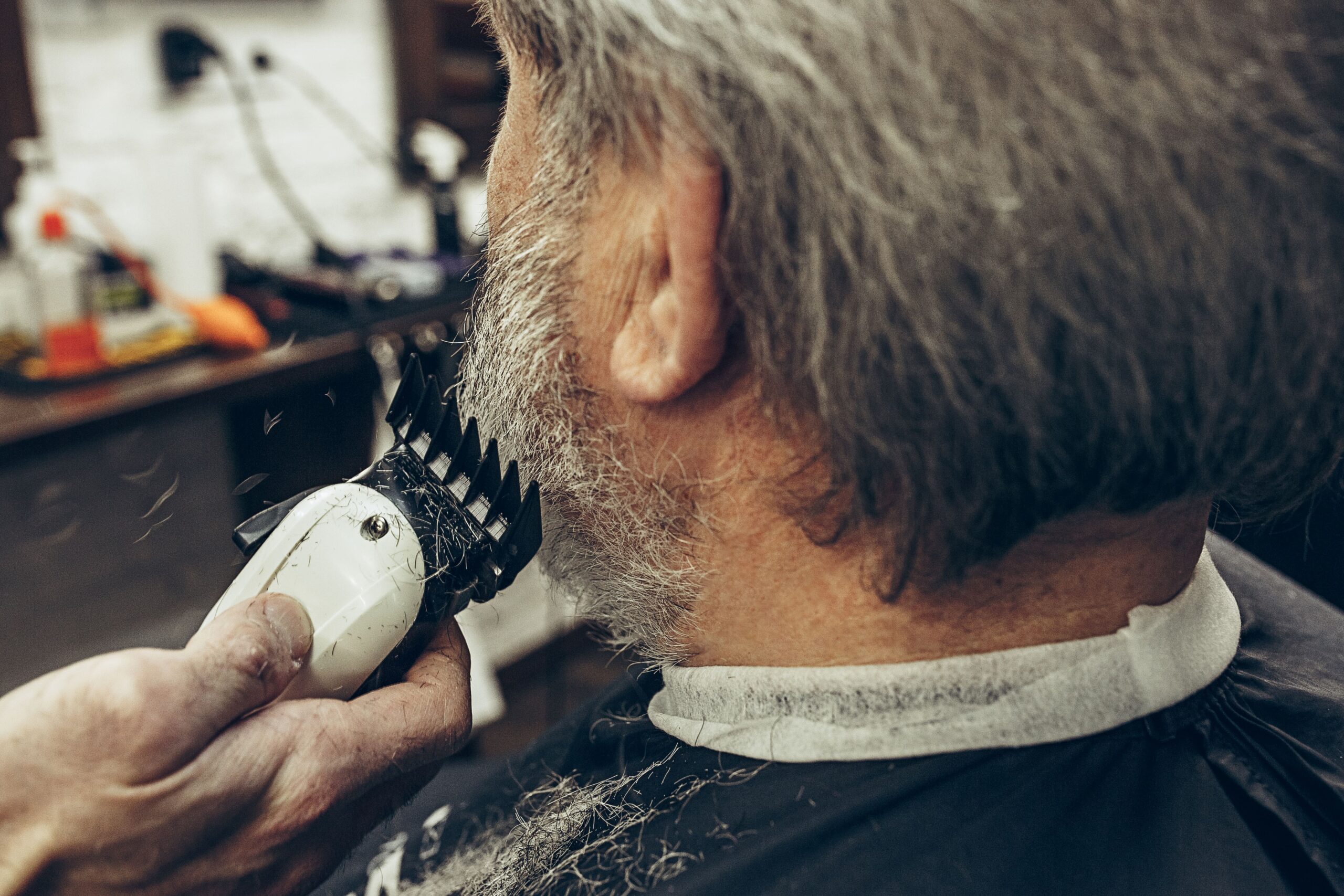 A professional barber in Larnaca trimming an older man's beard using high-quality electric clippers in a well-equipped barbershop.