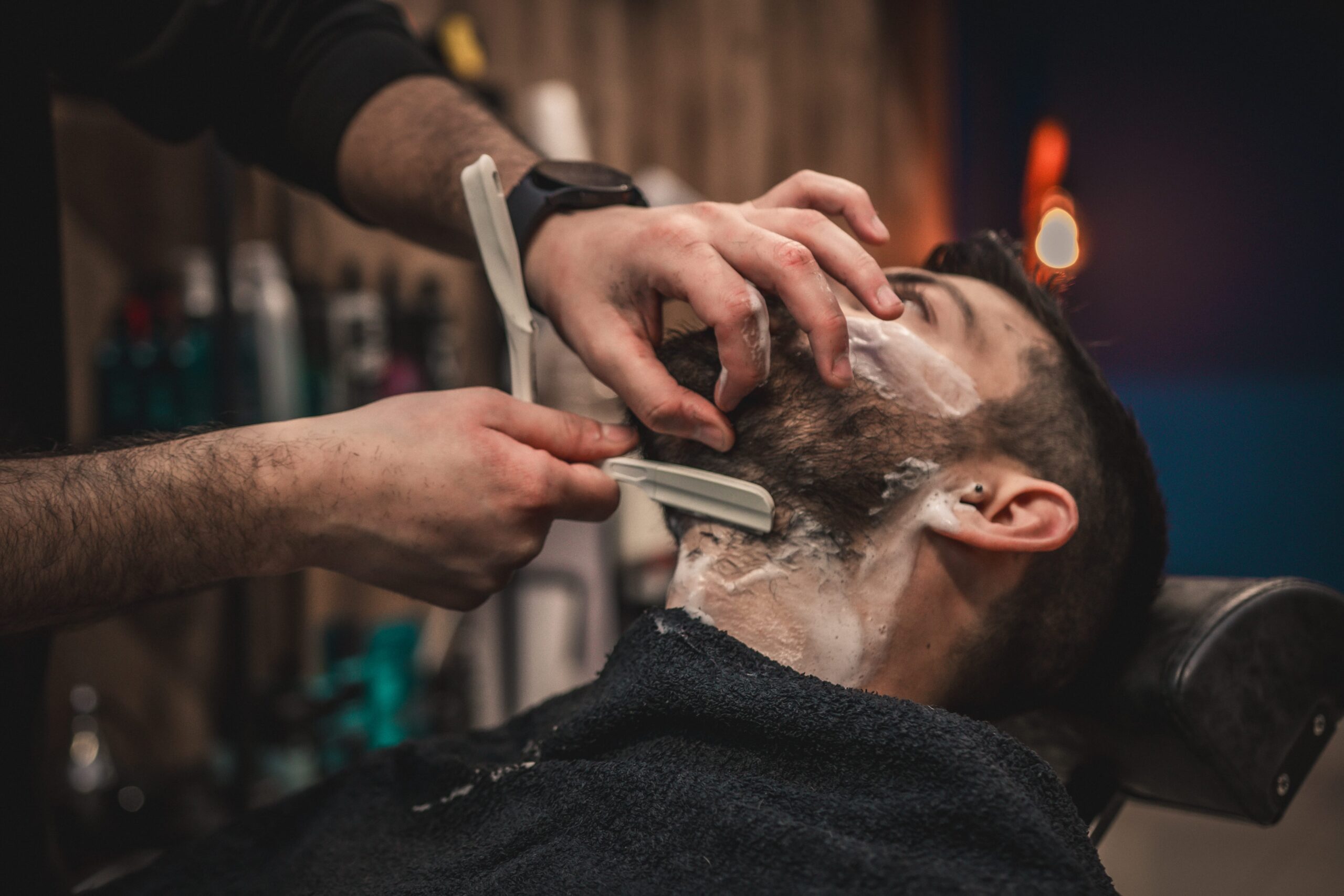 A professional barber in Larnaca performing a traditional wet shave with a straight razor, shaping a client’s beard using premium grooming products.