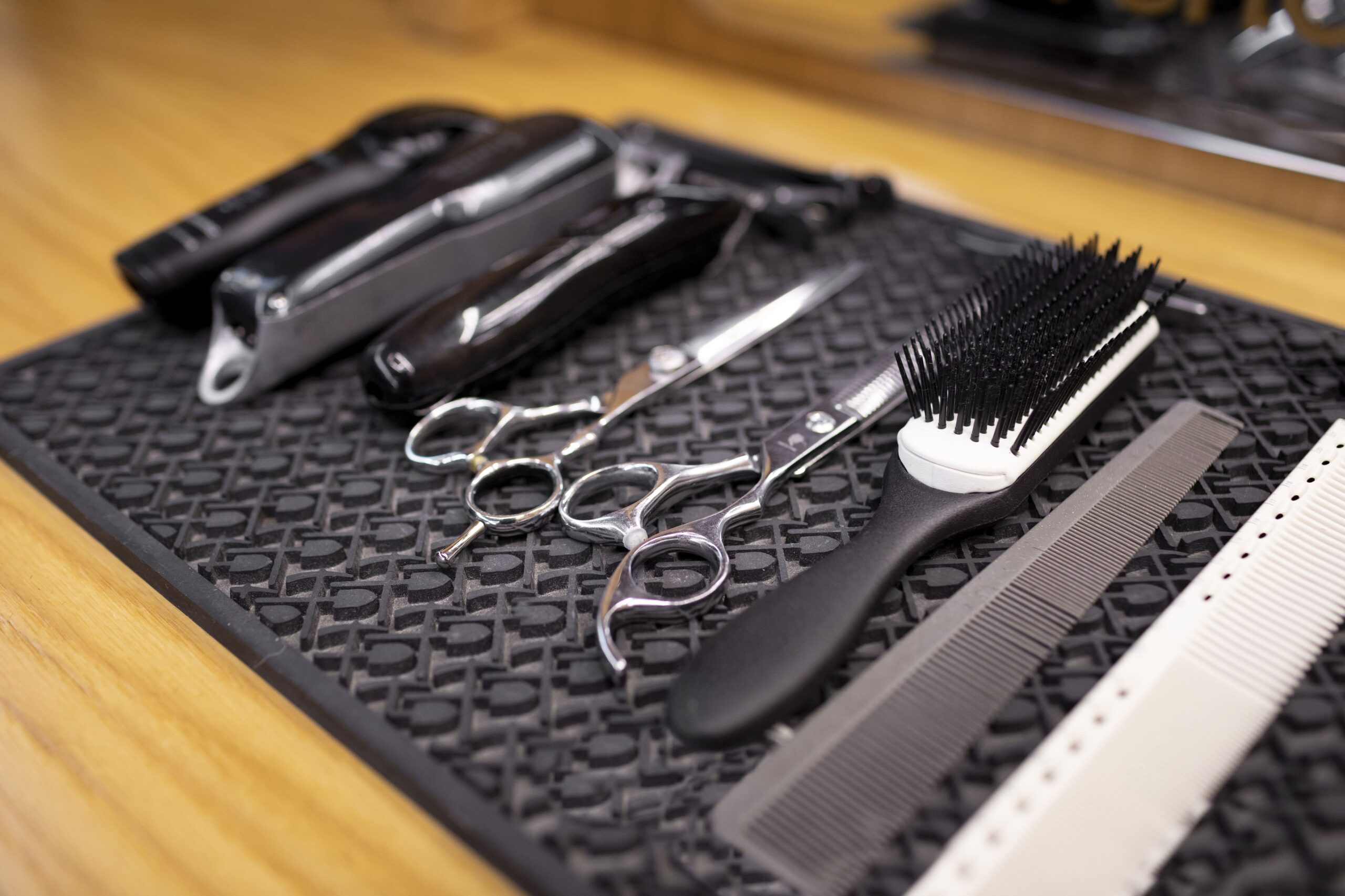 A set of barber tools, including hair clippers, scissors, brushes, and combs, arranged on a workstation.