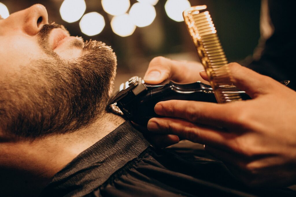 A barber using a gold comb and electric clippers to trim a man's beard.