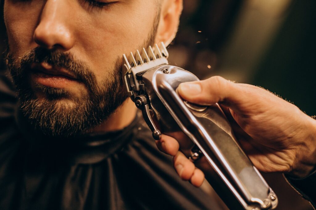 A barber in Cyprus trimming a man's beard with electric clippers.