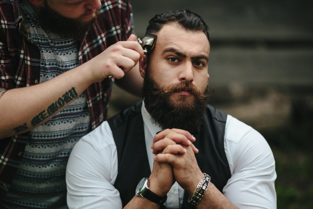 A barber using manual hair clippers to trim a well-groomed man's hair outdoors.