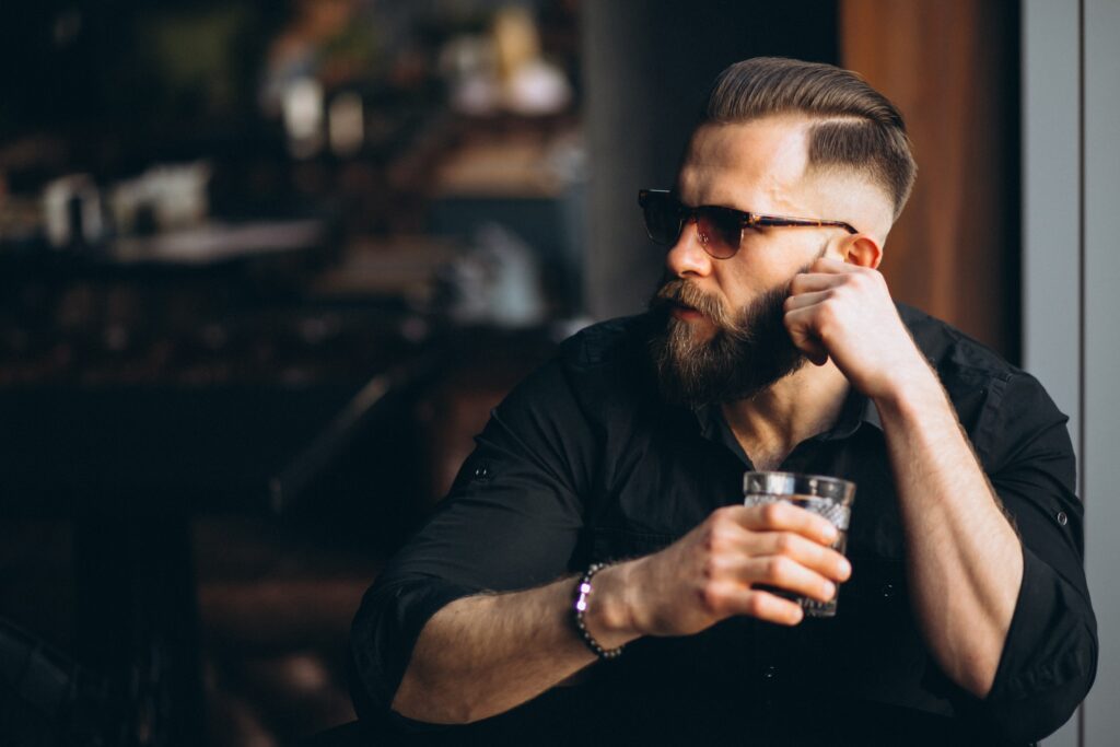 Bearded man with sunglasses enjoying a drink at a stylish Larnaca barber shop