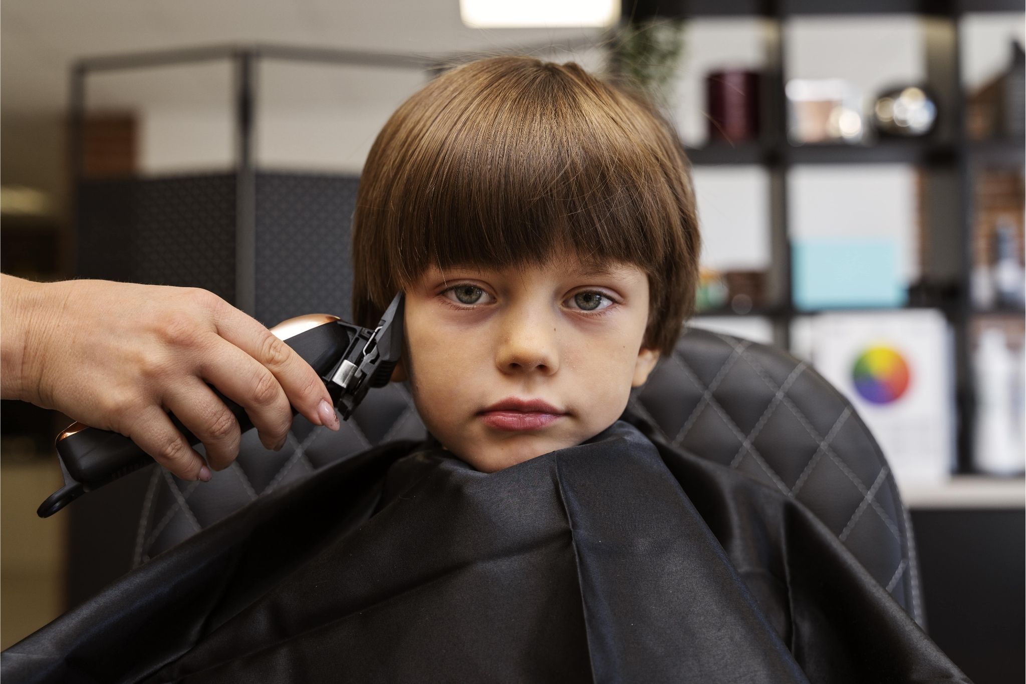 Young boy getting a haircut with clippers at a salon, showing one of the best hairstyles for kids.